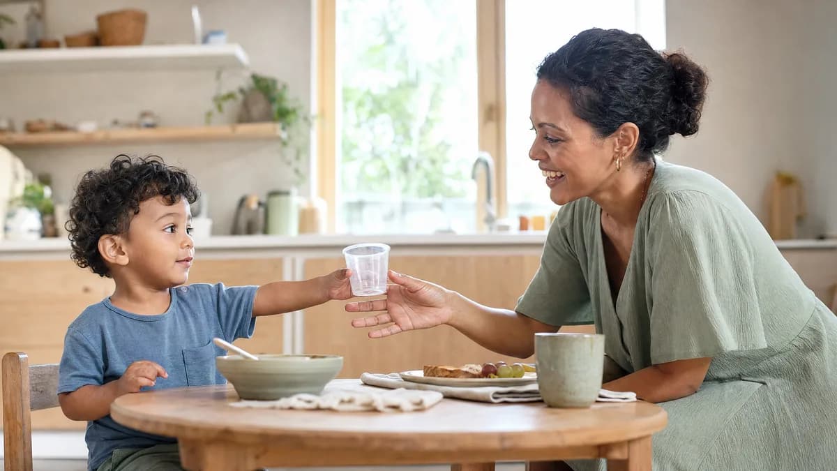 Un niño pequeño le ofrece un vaso vacío a su madre, que se agacha sonriendo para tomarlo.
